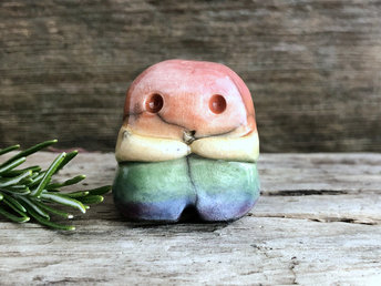 A sweet little nature spirit ceramic guardian statue glazed in rainbow colours and with a lovely, gentle face and little arms. It has a small branch design carved up one side.
