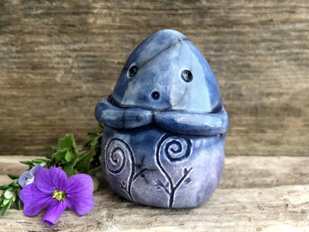 vaguely dome-shaped nature spirit ceramic sculpture. it is glazed in a bottom-to-top gradient of violet to deep blues and has spiral carvings on its body. it also has a gentle face, and two little arms across its front.