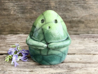 raku ceramic vaguely dome-shaped nature spirit sculpture. it is glazed in a gradient from forest green to spring green (bottom to top). it has sweet praying hands and an ooooo expression on its gentle face.