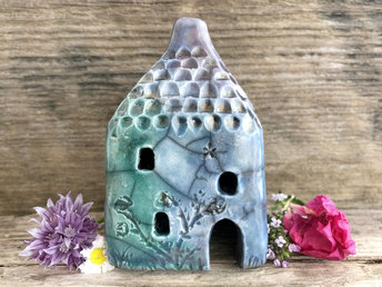 Raku ceramic kurinuki cottage glazed in forest green, blue, indigo, and violet. It has a cute little chimney, plant carvings on its walls, a cute door and lots of little windows.