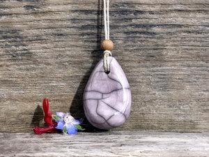 Raku ceramic worry pendant shaped a little like a bendy pear and glazed in pale purple. It has a sandalwood bead above it and is strung on a flax cord.
