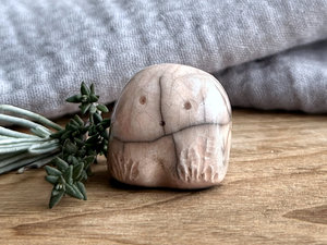 a small and stout nature spirit raku sculpture glazed in very pale peach. it has a cute little face, and flower and plant carvings on its front.