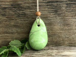 Raku ceramic worry pendant shaped a little like a bendy pear and glazed in light green. It has a sandalwood bead above it and is strung on a flax cord.