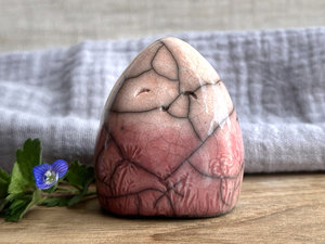 vaguely dome-shaped nature spirit ceramic sculpture. it is glazed in a bottom-to-top gradient of a soft bordeaux red to soft peach and has plant and flower carvings on its body. it also has a gentle, smiling face.