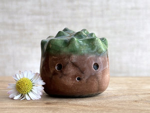 a roundish raku scuplture glazed in warm brown with green for the chestnut spikes on the top of its head. (they're not sharp at all!). it has a cute, open, friendly face.