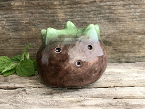 A round, chestnut-shaped raku scuplture glazed in warm brown with a bit of green for the chestnut spikes on the top of its head. (They're not sharp at all!). It has a cute, open, friendly face.