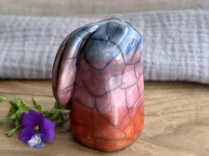 Raku ceramic usagi rabbit kami nature spirit glazed in a bottom-to-top gradient of burnt orange to mauve to blue-violet. Its ears are folded down its back, and it has a kind, gentle face.