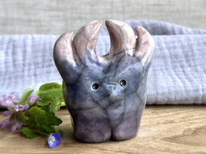 a raku ceramic creature. it has four stubby legs and gets wider as its body goes up. it eventually ends in four small antlers. on the way, it has a gentle face with a cute little nose. it's glaze in a bottom-to-top gradient of dark purple to grey-blue to a pale red-pink for the antlers. it is a friend.