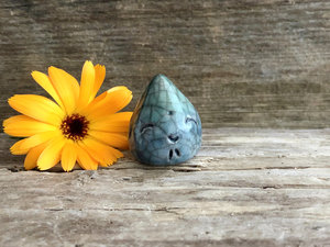 A very small raindrop raku ceramic sculpture glazed in blue and aqua green with a smiley face. A prayer to end the droughts and floods.