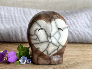 Ceramic raku owl kami nature spirit sculpture glazed mostly in soft brown with a white heart-shaped face. It has a very kind, friendly expression.