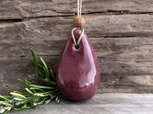 Raku ceramic worry pendant shaped a little like a bendy pear and glazed in a deep Bordeaux red-pink. It has a sandalwood bead above it and is strung on a flax cord.