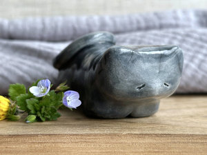 Little raku ceramic cat spirit kami sculpture glazed in grey. It has a kind, gentle, sleepy face, and its tail is curled over its back on its right.