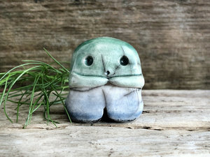 A sweet little nature spirit ceramic guardian statue glazed in the men's gay flag green, white, and blue colours and with a lovely, gentle face and little arms. It has a small branch design carved up one side.