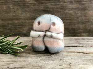 A sweet little nature spirit ceramic guardian statue glazed in the transgender pink, white, and blue colours and with a lovely, gentle face and little arms. It has a small branch design carved up one side.