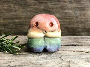 A sweet little nature spirit ceramic guardian statue glazed in rainbow colours and with a lovely, gentle face and little arms. It has a small branch design carved up one side.