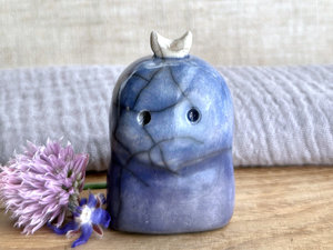 A kodama nature and forest spirit kami ceramic raku sculpture glazed in a bottom-to-top gradient of indigo-violet to blue. It has a gentle face, and a white crescent moon on its head.