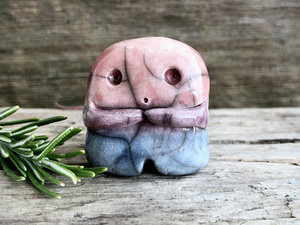 A sweet little nature spirit ceramic guardian statue glazed in the bisexual flag pink, purple, and blue colours and with a lovely, gentle face and little arms. It has a small branch design carved up one side.