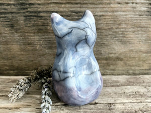 Raku ceramic sitting fox glazed in soft blue with a hint of purple at the bottom. He has a kind face, and a tail curled up his back.