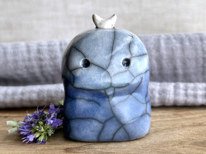 A kodama nature and forest spirit kami ceramic raku sculpture glazed in a bottom-to-top gradient of darker to lighter blue. It has a gentle-but-worried face, and a white crescent moon on its head.