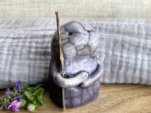 raku ceramic nature spirit warrior sculpture. it is glazed in a bottom-to-top gradient of violet to pale violet and carries a brown stick in one of its arms. it has a sad and worried but determined look on its gentle face.