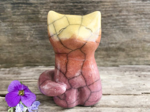Raku ceramic sitting fox glazed in a gradient from mauve to orange to golden yellow (bottom to top). It has a kind face, and its tail is curled around it.
