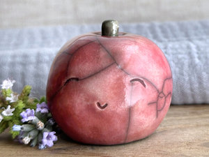 raku ceramic warm-red apple nature spirit sculpture with a happy, gently smiling face. it has a cute little green-brown stalk on top.