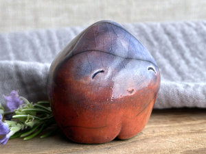 a vaguely dome-shaped nature spirit ceramic sculpture with a gently pointed head and four stubby little legs. it is glazed in a bottom-to-top gradient of warm red-orange to purple to blue with hints of violet and mauve throughout, and it has a very gentle, smiling face.