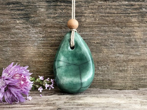 Raku ceramic worry pendant shaped a little like a bendy pear and glazed in forest green. It has a sandalwood bead above it and is strung on a flax cord.