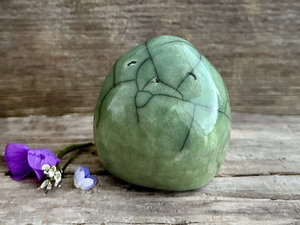 raku ceramic nature spirit sculpture glaze in a bottom-to-top gradient of spring green to a slightly more bluey green. it's very round but slightly pointy on top and it has a cute and happy wee face.