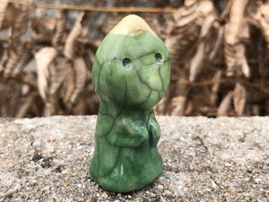 Ceramics raku sculpture of a leaf spirit. It is glazed in yellow at the top of its head, then spring green, then darker green, and it has a gentle, innocent face and two sweet little arms.