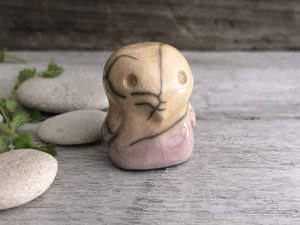 Ceramic raku sculpture of a sweet baby bird. He is glazed in soft, pale orange and mauve, and he has cute little wings.