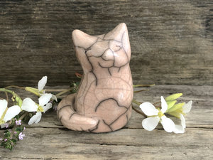 Raku ceramic sitting fox glazed in a soft warm peach colour. Her head is uplifted gently toward the sky, and she has a very sweet face.