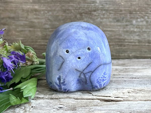 a small and stout nature spirit raku sculpture glazed in blue. it has a cute little face, and flower and plant carvings on its front.