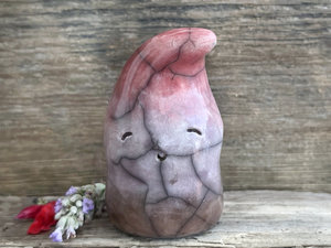 raku ceramic gnome spirit glazed in a bottom-to-top gradient of brown to soft purple to soft bordeaux red. it has a happy, gentle, kind face, and the top of its head is curled over, a little like it's wearing a nightcap.