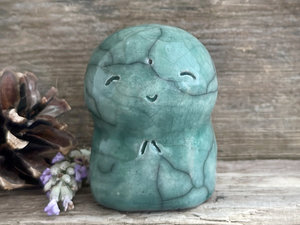 a smiley and loving Jizo Shinto raku ceramic sculpture talisman glazed in forest green. they have a kind, gentle face and are a wonderful smooth shape to hold in the hand.