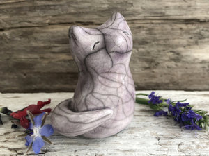 Raku ceramic sitting fox glazed in a soft warm purple colour. His head is uplifted gently toward the sky, and he has a very sweet face.