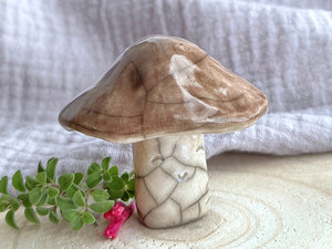 Cute mushroom raku ceramic sculpture with a very smiley face. His stalk is glazed in creamy-white (this is where his face is) and his mushroom cap is brown.