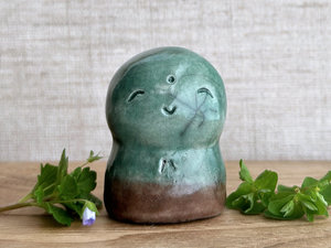 a smiley and loving Jizo Shinto raku ceramic sculpture talisman glazed in forest green and brown (at the bottom). they have a kind, gentle face and are a wonderful smooth shape to hold in the hand.