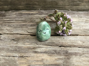 Tiny raku ceramic earth spirit glazed in a soft, pale spruce green. It is shaped a little like a bent over raindrop and has a very sweet face!
