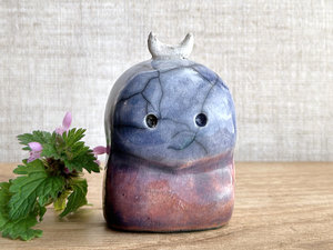 A kodama nature and forest spirit kodama kami ceramic raku sculpture glazed in a bottom-to-top gradient of red-orange to mauve to purple to indigo. It has a gentle face, and a white crescent moon on its head.