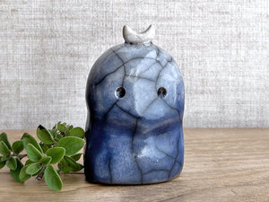 A kodama nature and forest spirit kami ceramic raku sculpture glazed in deep blue. It has a gentle face, and a white crescent moon on its head.