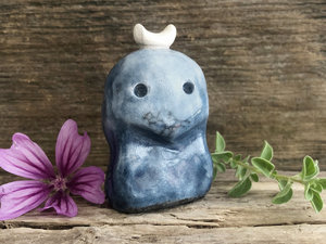 A kodama nature and forest spirit kami ceramic raku sculpture glazed in shades of blue with a gentle face and a white crescent moon on its head.
