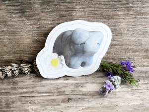 a sticker of a pale blue raku cermic bear sculpture. it has a sweet, friendly face, and there is a daisy next to it (part of the sticker). there is a thin white border around the image of bear and daisy.