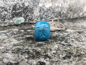 Little raku ceramic Shinto Jizo pendant glazed in a turqouise colour and hung from an adjustable eco hemp cord. Jizo is shaped a little like a smooth pebble and has a happy, smiling face.