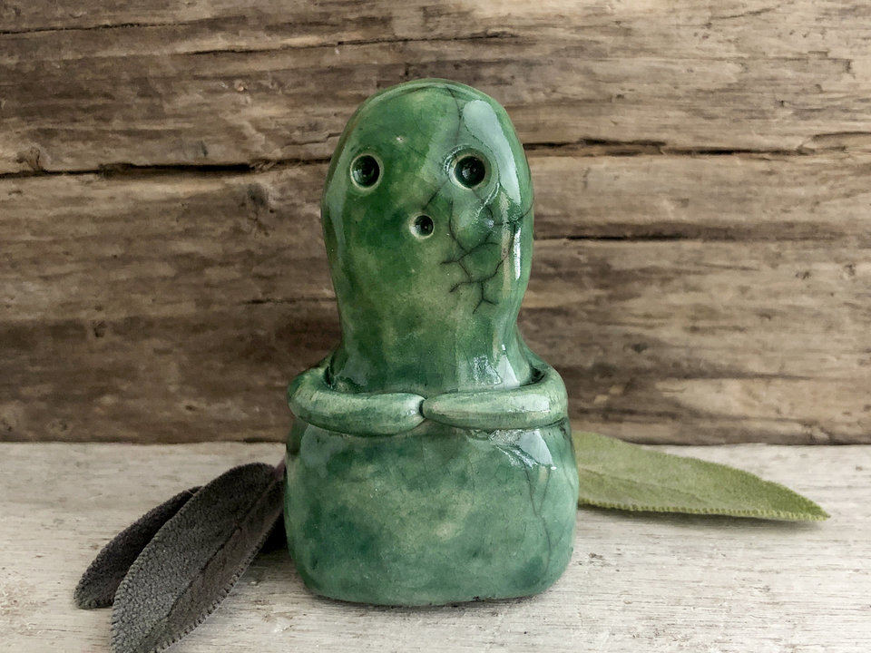A very sweet, tall kodama nature spirit ceramic guardian statue glazed in shades of green and with a lovely, gentle face and little arms.