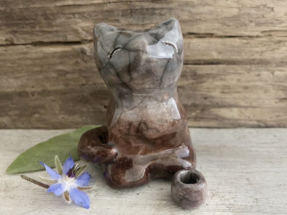 Raku ceramic sitting fox glazed in soft gradient from brown to a greyish blue. He has a kind face, the impression of two little arms across his front, and looks like he's sitting cross-legged.