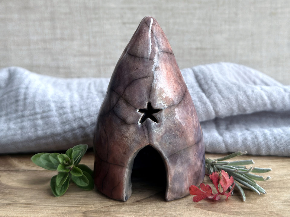 Raku spirit cave with with an arched door, a star window above it, and another window around the side. It's glazed in a variety of colours: soft warm orange, violet and purple, indigo, mauve, and soft deep red.