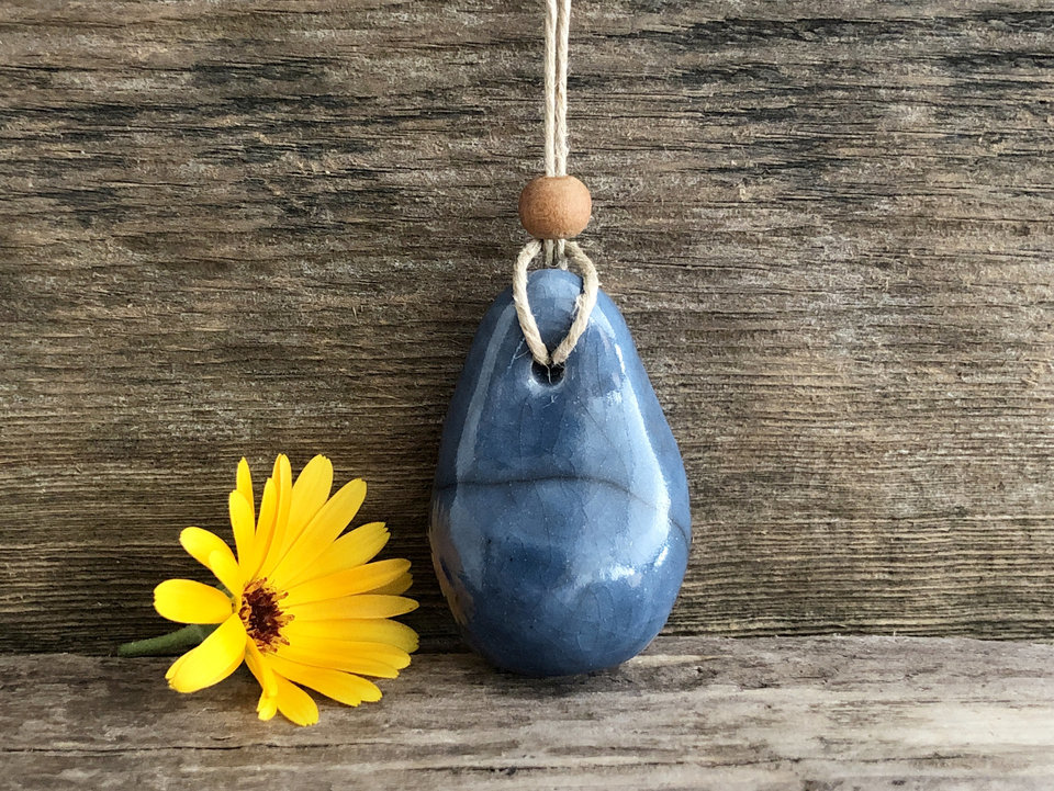Raku ceramic worry pendant shaped a little like a bendy pear and glazed in blue. It has a sandalwood bead above it and is strung on a flax cord.