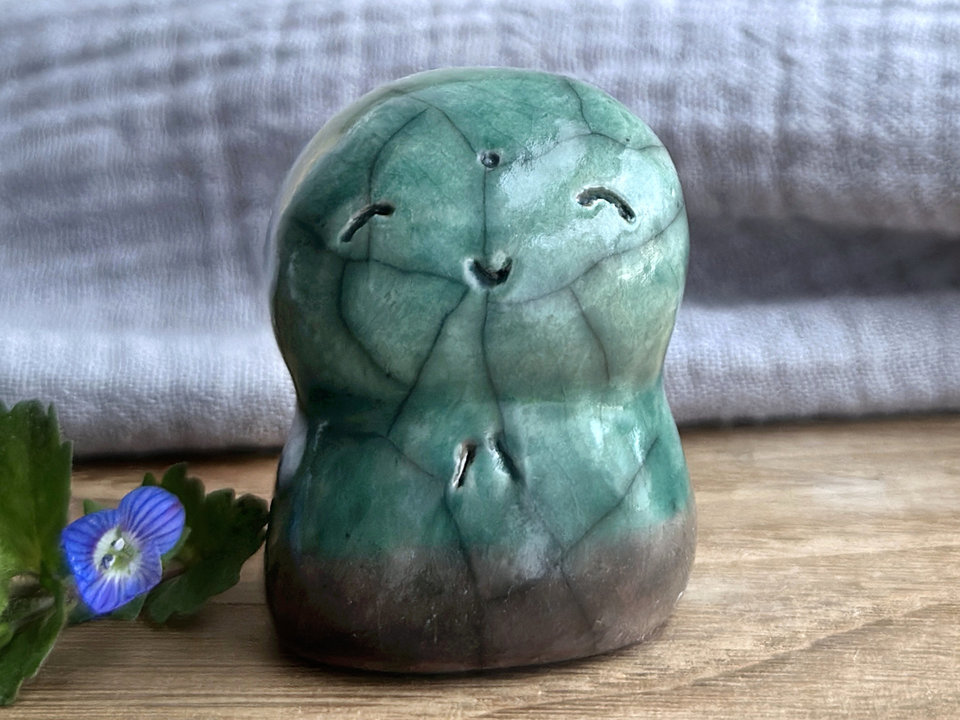 a smiley and loving Jizo Shinto raku ceramic sculpture talisman glazed in forest green and brown (at the bottom). they have a kind, gentle face and are a wonderful smooth shape to hold in the hand.