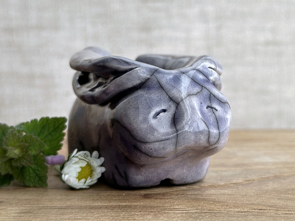 Raku ceramic sculpture of a rabbit. It is sitting with its long ears folded down its back and is glazed in a soft lavender colour. It has a very sweet, gentle face.